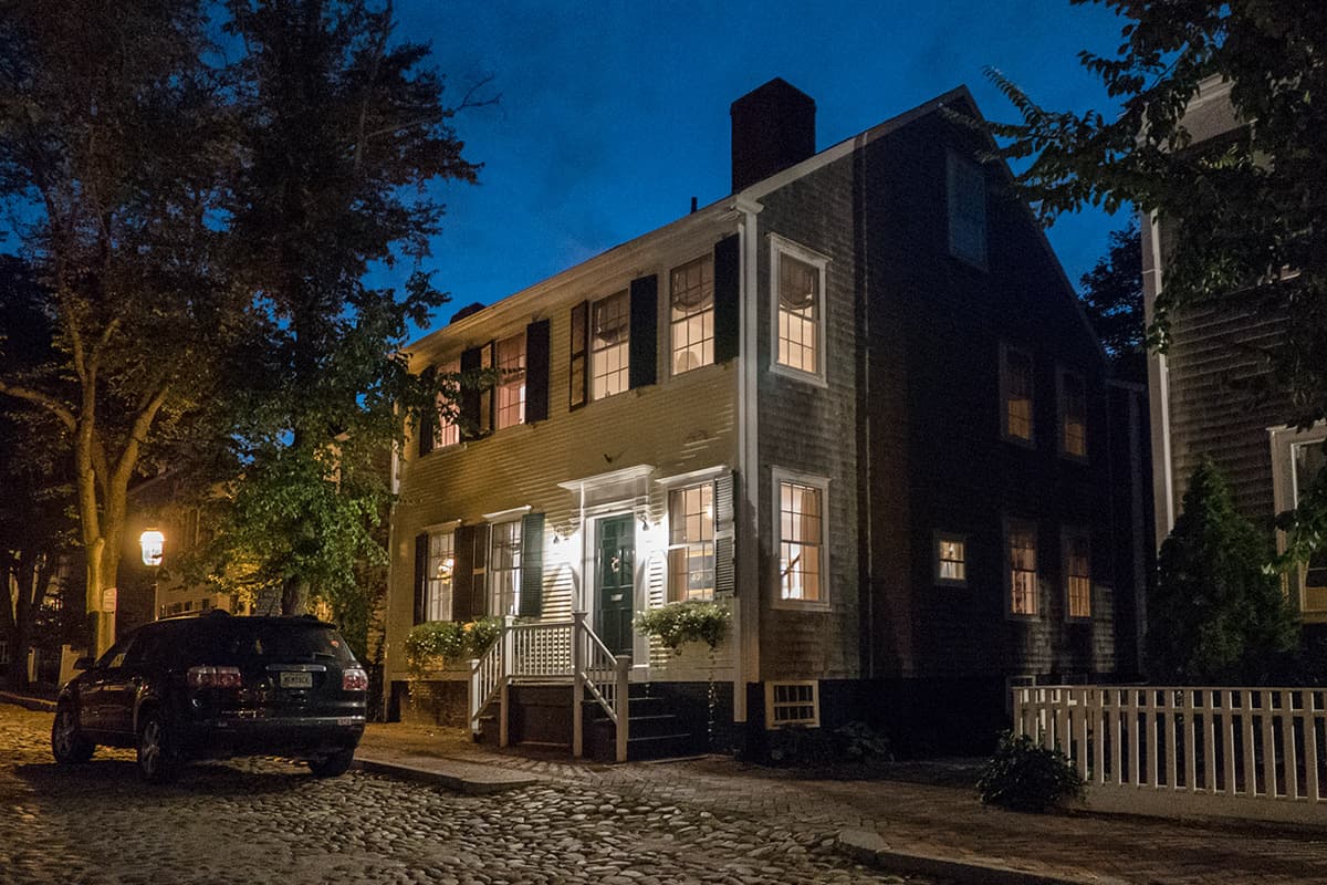 The 1830 whaling captain's house at night from the cobbled street, lit windows and lanterns at the front door