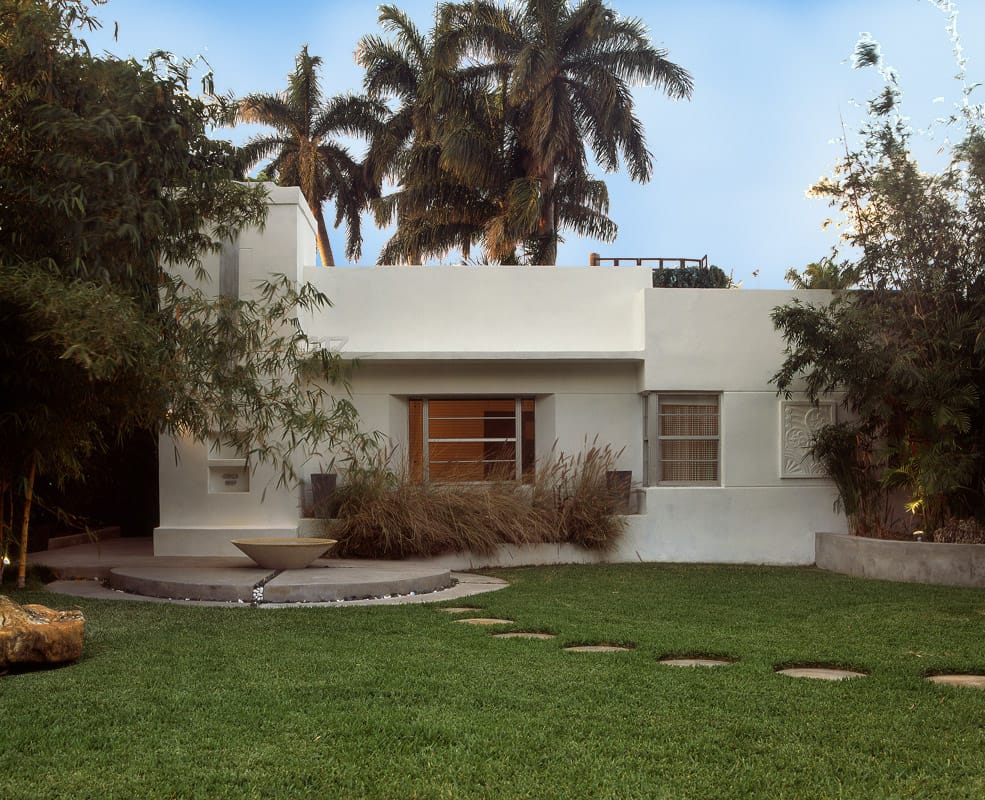 The white stucco Art Deco cottage at dusk behind clipped lawn, with royal palms overhead and a round step to the front door