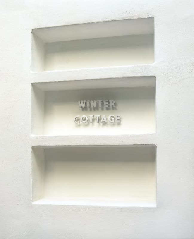 Three rectangular niches cut into the white plaster wall, the middle one holding the cast letters that read Winter Cottage