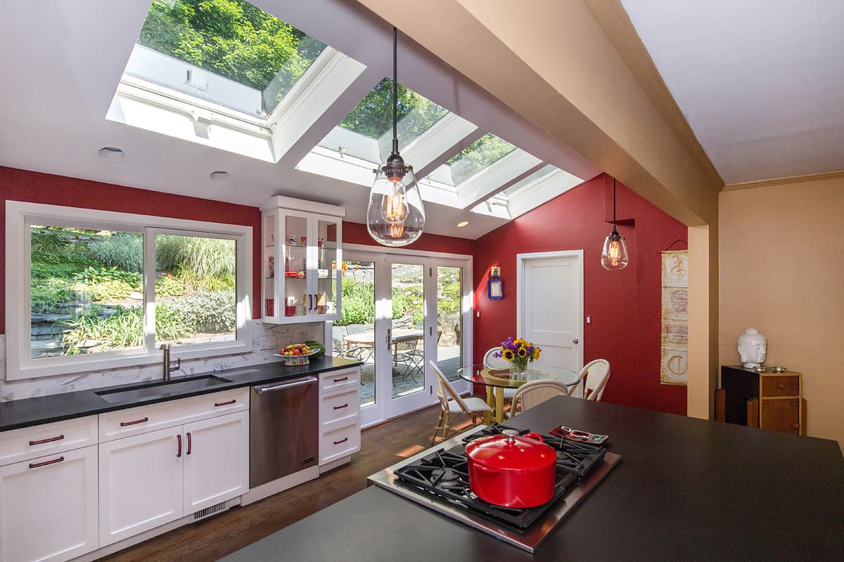 Kitchen of the contemporary Westchester house, deep red walls under a vault of skylights with black counters and white cabinets