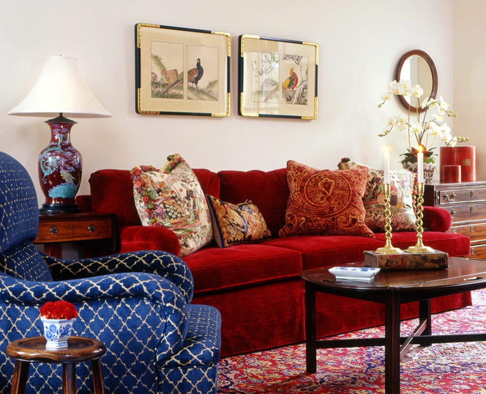 Red velvet sofa under a pair of framed Asian bird paintings, an indigo lattice armchair in front, orchids and a Chinese vase lamp alongside
