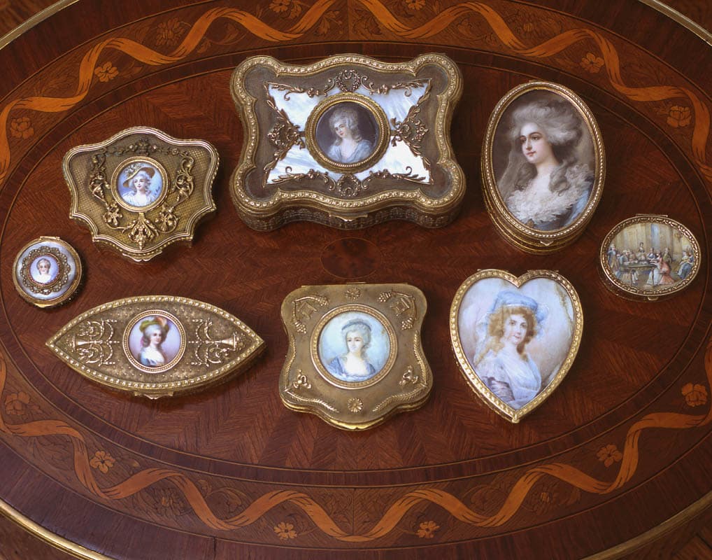 Eight enamel and gilt boxes set out on an oval marquetry table, each with a painted portrait miniature of a woman, one heart shaped and one oval with a pearled border