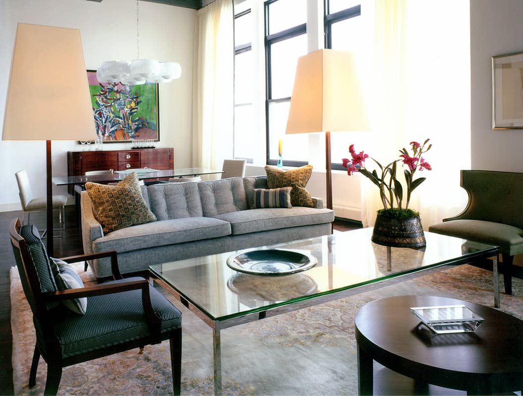 Tribeca loft living room, a grey flannel sofa between two tall shaded floor lamps with a chrome and glass table on a faded carpet