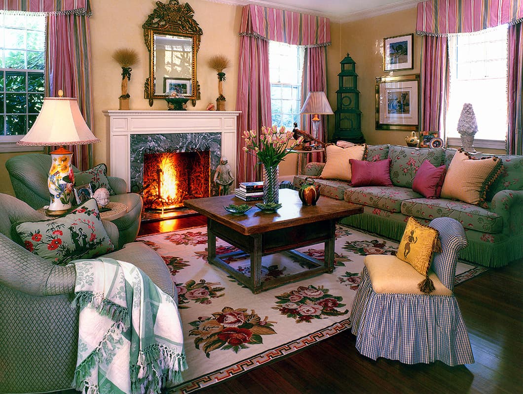 Living room of the 1890 Victorian cottage in Larchmont, a lit fire under a white mantel and gilt mirror with a rose chintz sofa