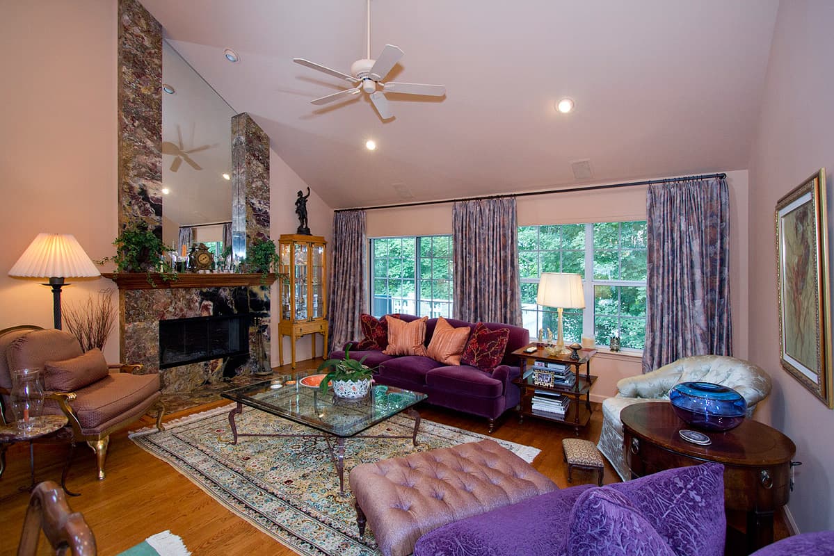 Vaulted living room of the Westchester townhouse, a full height marble chimneybreast and mirror with a purple velvet sofa on a floral carpet