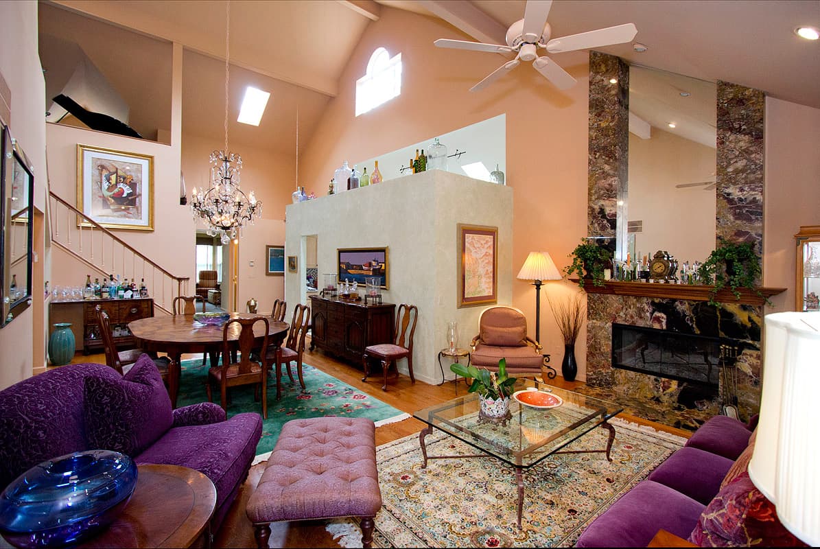 The full length of the vaulted main floor: purple velvet seating and a glass table in front, the dining table and stair beyond, a crystal chandelier, and the plaster partition topped with old glass under the skylights