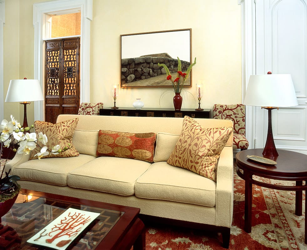 Townhouse parlour with a cream boucle sofa and crimson vine cushions, a photograph of a dry stone wall over a black Chinese chest and carved fretwork doors to the hall